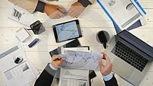 Male hands of two successful business partners examining graphs and discussing financial reports in office. Young