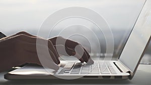 Male hands typing and using touchpad on laptop computer keyboard against window in office. Business concept