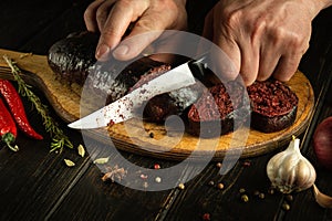 Male hands use a knife to cut blood sausage on a cutting board. Preparing a national dish on the kitchen table