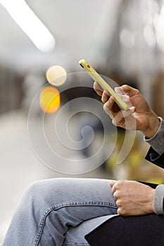 Male hands using cellphone/smartphone in yellow case at subway