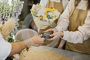 Male hands using credit card paying for purchase using payment terminal in flower shop