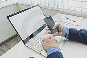 Male hands using smartphone mockup with blank screen at office desk with an open laptop mockup and tablet computer. For