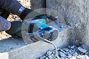 Male hands wearing safety gloves are drilling a wall with a rotary electric drill-hammer, outdoors