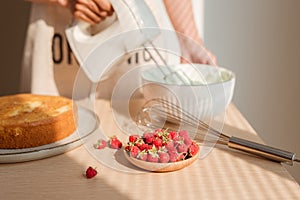 Male hands whipping whites cream in glass bowl with mixer on wooden table. Making sponge cake or red velvet cake