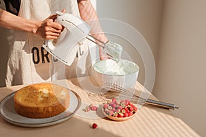 Male hands whipping whites cream in glass bowl with mixer on wooden table. Making sponge cake or red velvet cake