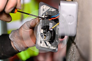 Male hands wiring a uk socket plug on garage wall with screw driver photo