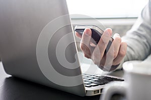 Male hands working on Laptop and holding a smart phone on the desk.