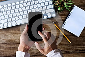 Male hands working smartphone and laptop. Office desktop on wooden table  background