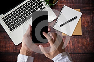 Male hands working smartphone on modern laptop. Office desktop on wooden table  background
