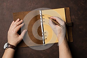 Male hands writing in diary on brown background