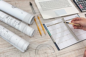 Male hands writing on notepad with part of industrial blueprint with calculator, tools and laptop