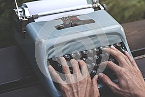 Male hands writing with an old blue typewriter
