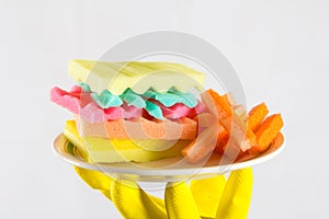 Male hands in yelliw gloves holding a burger made from sponges different colors. Concept of unhealthy food and non