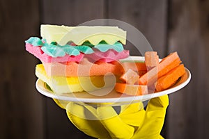 Male hands in yelliw gloves holding a burger made from sponges different colors. Concept of unhealthy food and non