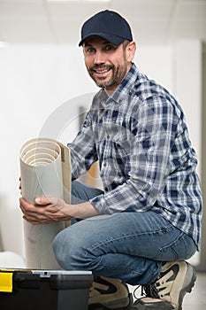 male handyman rolling carpet on floor at home