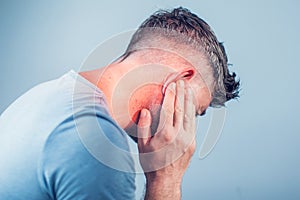 Male having ear pain touching his painful head on gray photo