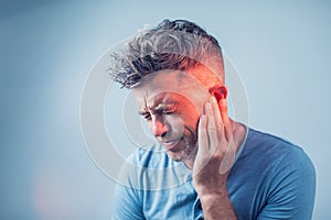 Male having ear pain touching his painful head on gray photo