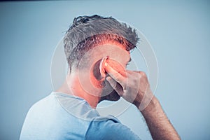 Male having ear pain touching his painful head on gray