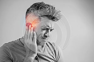 Male having ear pain touching his painful head isolated on gray