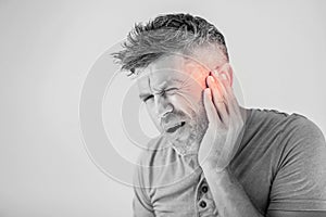 Male having ear pain touching his painful head isolated on gray