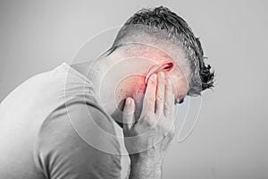 Male having ear pain touching his painful head isolated on gray photo