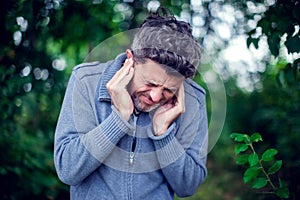 Male having ear pain touching his painful head outdoor photo