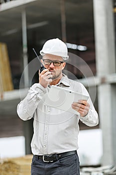 Male head engineer wearing white safety hardhat with walkie talk