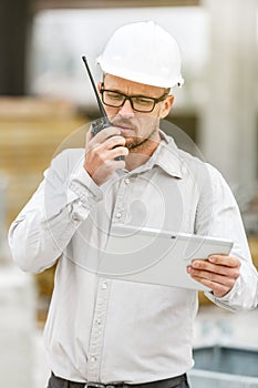 Male head engineer wearing white safety hardhat with walkie talk