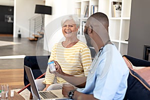 Male health worker with laptop discussing with caucasian senior woman over medication dose