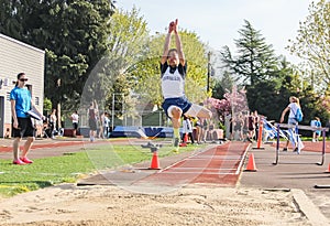 Male High school athlete at peak of long jump in track meet