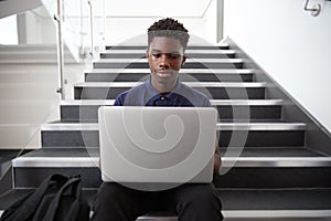 Male High School Student Sitting On Staircase And Using Laptop