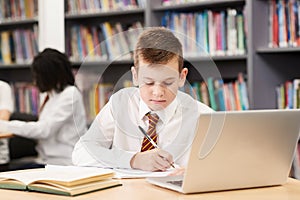 Male High School Student Wearing Uniform Working At Laptop In Li