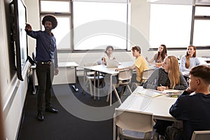 Male High School Teacher Standing Next To Interactive Whiteboard And Teaching Lesson