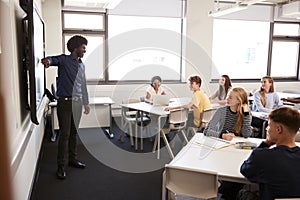 Male High School Teacher Standing Next To Interactive Whiteboard And Teaching Lesson