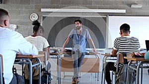 Male high school teacher walking in class talks to teen student answering question. Student raising hand. 4k video.