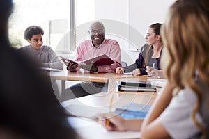 Male High School Tutor Sitting With Students At Desk In Class