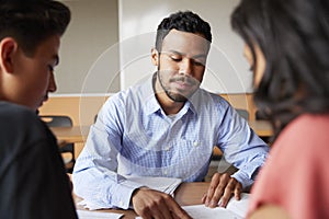 Male High School Tutor With Two Students At Desk In Seminar
