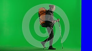 A male hiker with a hiking backpack on his back, and trekking poles walks to the side and disappears behind a screen