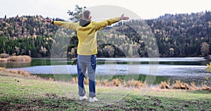 Male hiker raising his hands up and looking happy near lake in national park