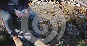 Male hiker resting, relaxing sitting on stone on beautiful mountain river shore after hard trek in highlands. Traveler