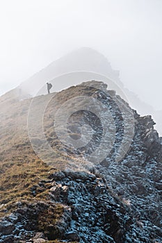 Male hiker stands atop a fog-covered mountain, admiring the view of the surrounding landscape