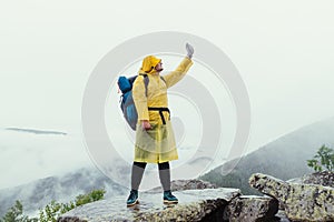 Male hiker on top of a mountain on a rock in rainy weather catches a net on a smartphone on a background of cloudy mountains