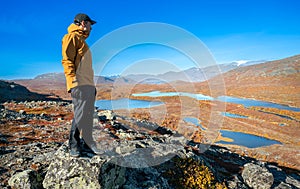 Male hiker in yellow hardshell jacket and black pants overlooking epic view of vast arctic landscape of Stora Sjofallet