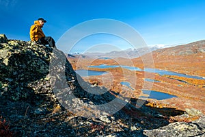 Male hiker in yellow hardshell jacket and black pants overlooking epic view of vast arctic landscape of Stora Sjofallet