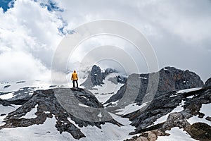 Male hiker with yellow raincoat  standing on top of mountain.