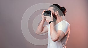 Male hipster is taking a photo while holding camera near face. Side view.