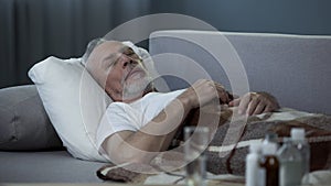 Male in his 60s sleeping in bed at home, pills and fluids standing on the table