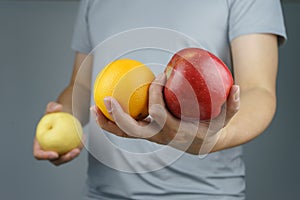 Male holding the apple and orange in one hand, and pear in another hand. It is a vegetarian and vegan food concept