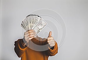 Male holding spread stack of 50 US dollars and making thumbs up sign with copy space