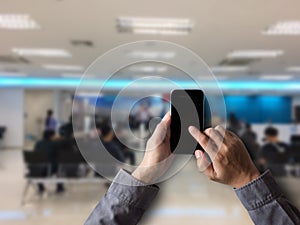 Male holding white mobile phone with blank white screen in bank.